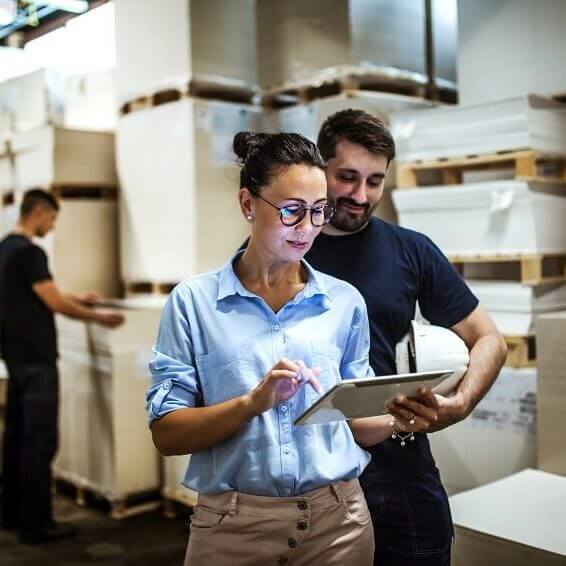 Two people working inside a warehouse and looking at a tablet.