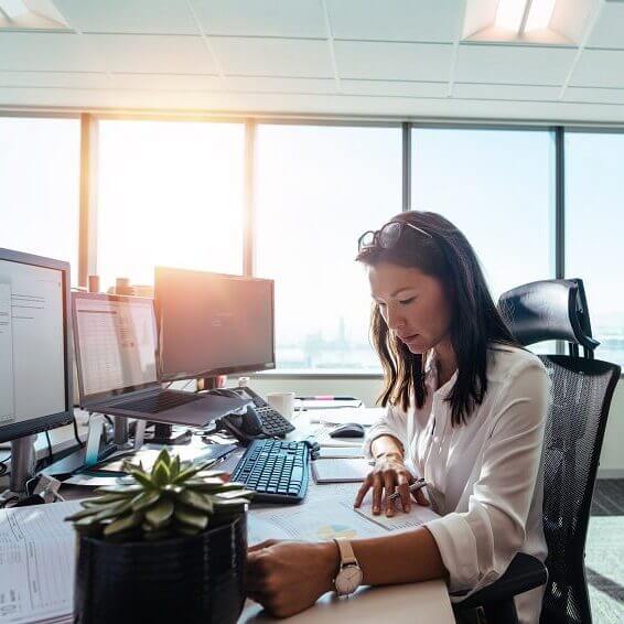 A woman working in an office and sitting at a desk reviewing a sheet of numbers or charts.