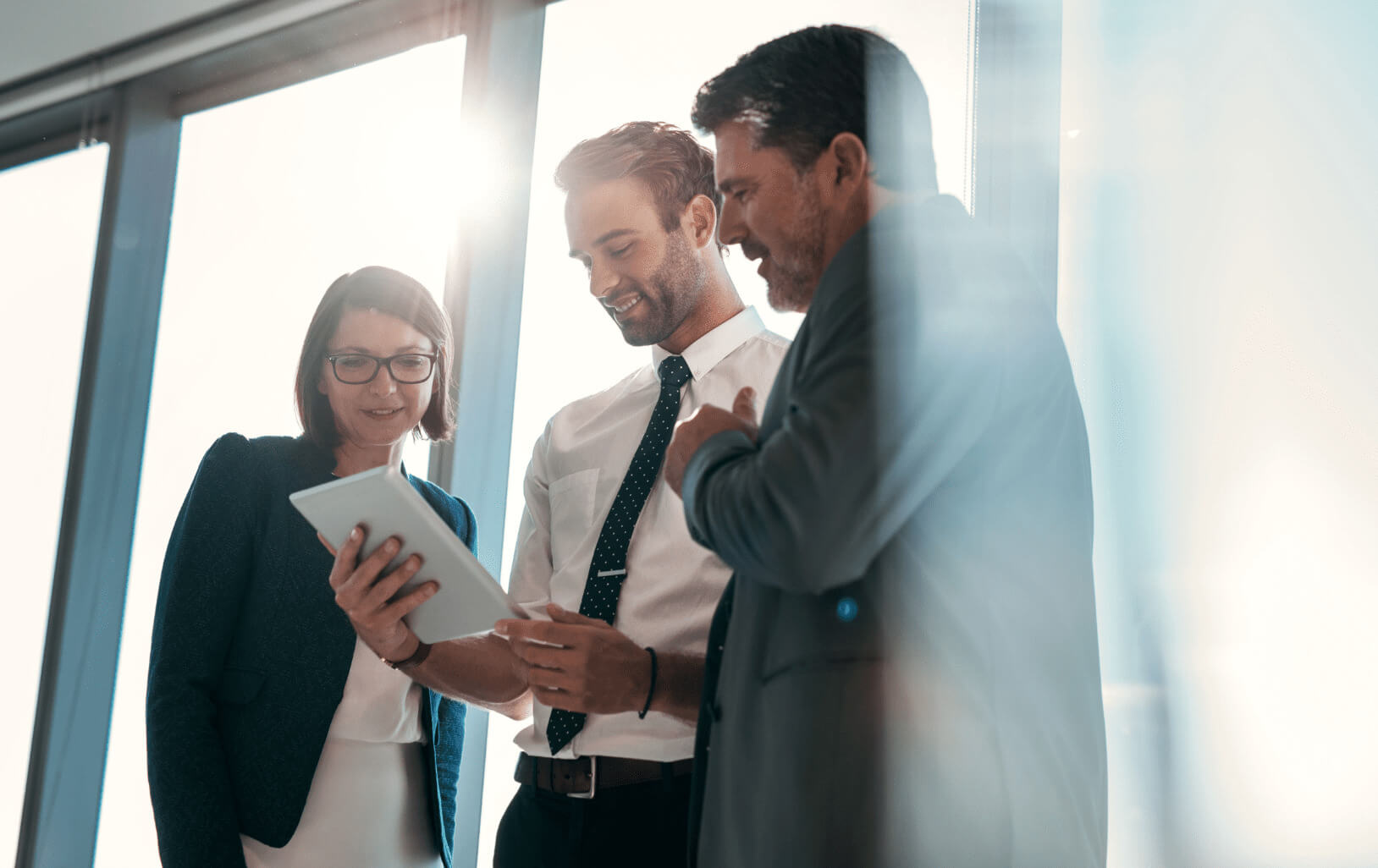 Three people in an office environment reviewing information a tablet.