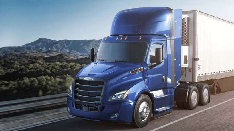 A tractor-trailer driving on the right lane of a road with mountains in the background.