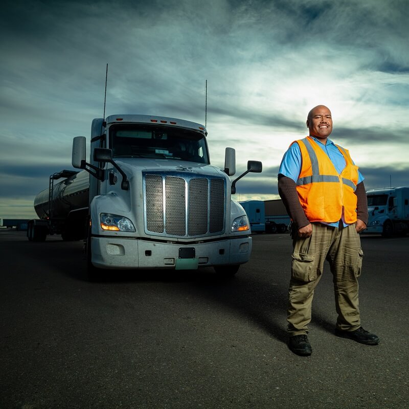 A truck driver wearing a hi-vis vest in front of a cab and tanker trailer.